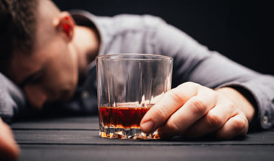 Пьяный мужчина со стаканом алкоголя спит за столом